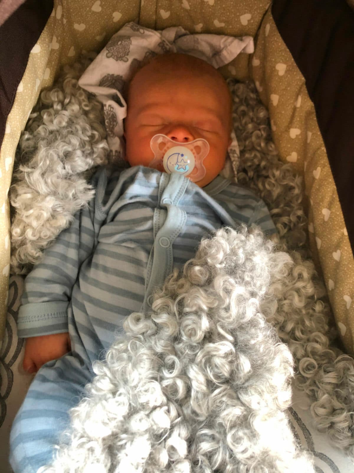Baby som sover på et krøllete lammeskinn i vogna.